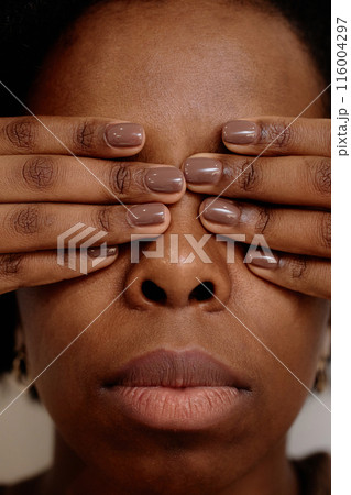 Vertical extreme close up on young Black woman covering eyes with hands in fear feeling hurt. Female African American experiencing abuse in relationship Vertical extreme close up on young Black woman covering eyes with hands in fear feeling hurt. Female African American experiencing abuse in relationship 116004297