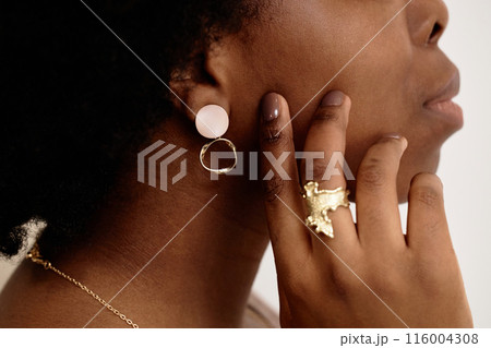 Cropped close up side view of unrecognizable Black woman wearing matching designer earrings and golden ring on white background Cropped close up side view of unrecognizable Black woman wearing matching designer earrings and golden ring on white background 116004308