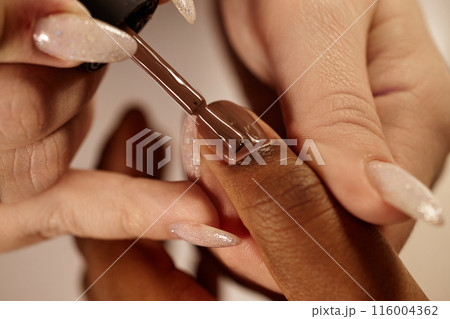 Close up of nail tech covering African American clients nails with brownish lacquer creating nude manicure in beauty studio Close up of nail tech covering African American clients nails with brownish lacquer creating nude manicure in beauty studio 116004362