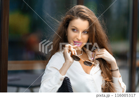 Close up outdoor portrait of a young stylish Caucasian woman sitting in sidewalk cafe. Close up outdoor portrait of a young stylish Caucasian woman sitting in sidewalk cafe. 116005317