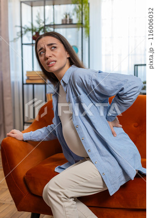 Upset ill young pregnant woman feeling sick suffering from lower back pain sitting on home sofa Upset ill young pregnant woman feeling sick suffering from lower back pain sitting on home sofa 116006032
