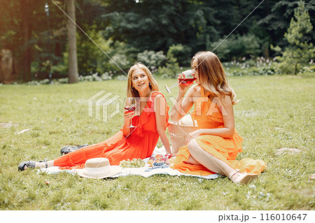 Beautiful girl in a red dress. Women sitting in a summer park. 116010647