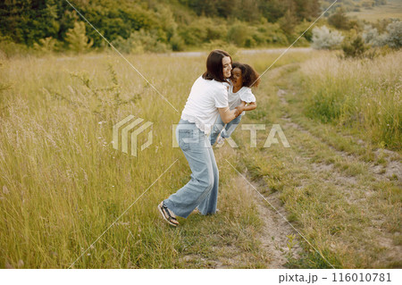Photo of caucasian mother and her african american daughter together. Girl has black curly hair. Mother and daugher wearing white t-shirts. 116010781