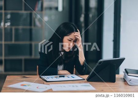 Young sad businesswoman is sitting at table, covering his face On desk is laptop, tablet computer, Stress. Serious woman concentrating on his paper work. 116010901