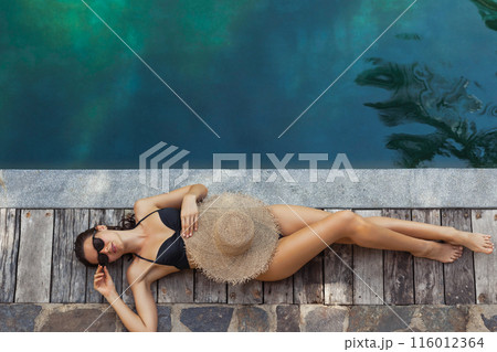 Woman Sunbathing by Pool with Sun Hat 116012364