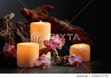 Orchid flowers, burning candles, and old wooden snags on a black background. Orchid flowers, burning candles, and old wooden snags on a black background. 116015730