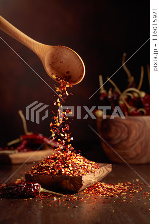 Chilli flakes are poured into a wooden dish. 116015921