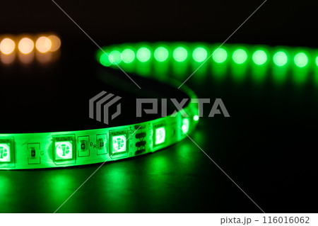 Bobbin with roll of glowing LED strip lighting placed on table, green and warm white color 116016062