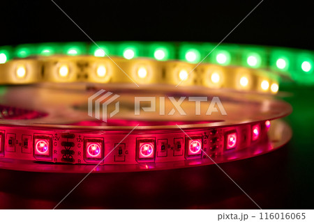 Bobbin with roll of glowing LED strip lighting placed on table, pink, green and warm white color 116016065