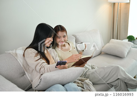 Happy Asian lesbian couple relaxing on couch and reading book together. LGBTQ people lifestyle concept Happy Asian lesbian couple relaxing on couch and reading book together. LGBTQ people lifestyle concept 116016993