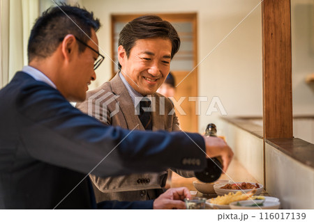 飲み屋のカウンターで上司や同僚にお酌する笑顔のビジネスマン 116017139