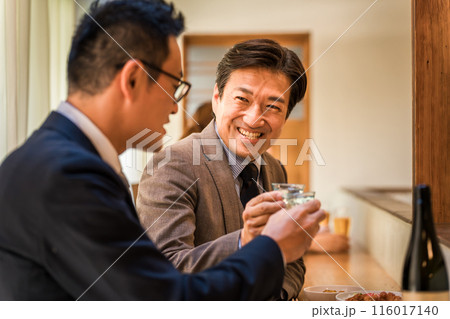 居酒屋・飲み屋のカウンターで部下と楽しくお酒を飲むビジネスマンの男性 116017140