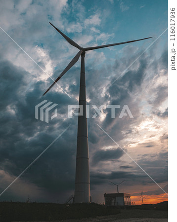 Bottom view of a tall wind turbine silhouette against dramatic sunset sky. 116017936