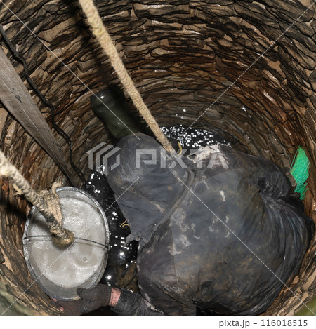 A man disinfects stones inside a well after cleaning the bottom. 116018515