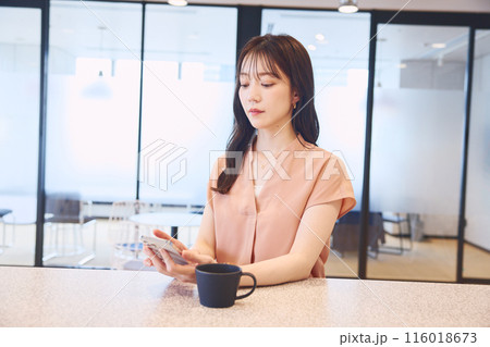 オフィスのパンドリーでスマホを見る女性 オフィスのパンドリーでスマホを見る女性 116018673