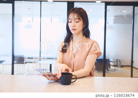 オフィスのパンドリーでスマホを見る女性 オフィスのパンドリーでスマホを見る女性 116018674