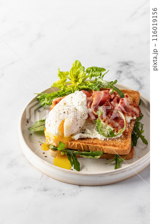 Toasts sandwich with poached egg, arugula, bacon and cream cheese on white plate marble background. Isolated, text space Toasts sandwich with poached egg, arugula, bacon and cream cheese on white plate marble background. Isolated, text space 116019156