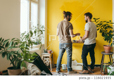 A married couple is painting the walls mustard yellow and decorating their new home. The color is warm. 116021935