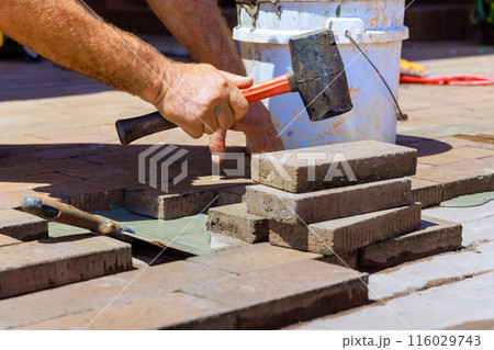 Employee is repairing footpath by replacing damaged bricks during reconstruction 116029743