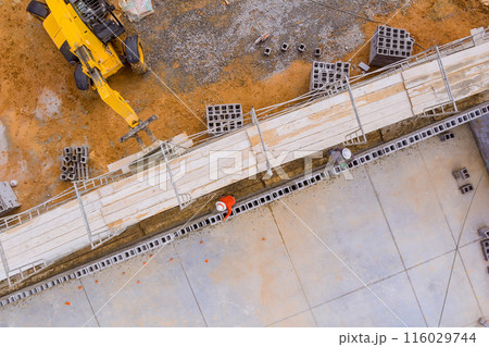 Standing on scaffold, bricklayer constructs working concrete wall from concrete blocks 116029744