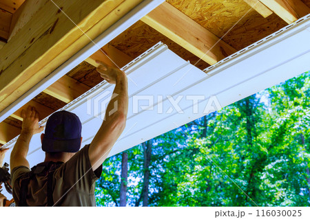 Having new employee install vinyl soffit plastic panels on facade ceiling of new house 116030025