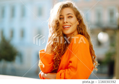 Young woman posing against backdrop of urban landscape in bright orange dress. Concept of lifestyle. Young woman posing against backdrop of urban landscape in bright orange dress. Concept of lifestyle. 116030392