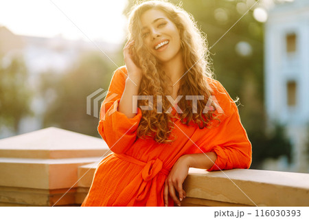 Young woman posing against backdrop of urban landscape in bright orange dress. Concept of lifestyle. Young woman posing against backdrop of urban landscape in bright orange dress. Concept of lifestyle. 116030393