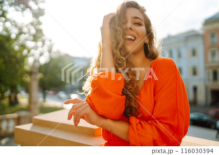Young woman posing against backdrop of urban landscape in bright orange dress. Concept of lifestyle. Young woman posing against backdrop of urban landscape in bright orange dress. Concept of lifestyle. 116030394
