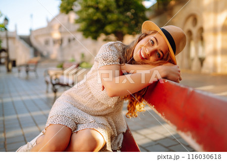 Happy young woman in hat at dawn enjoys view of beautiful buildings. Lifestyle, tourism concept. 116030618