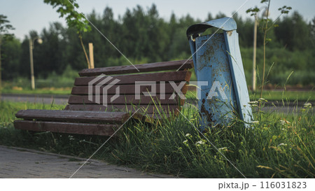 An old wooden bench next to a blue trash can 116031823