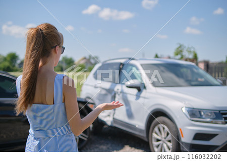 Sad young woman driver standing near her smashed car looking shocked on crashed vehicles in road accident Sad young woman driver standing near her smashed car looking shocked on crashed vehicles in road accident 116032202