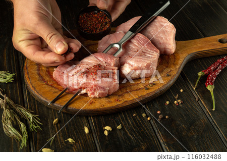 A chef is preparing a meat steak with aromatic spices on the kitchen table in a restaurant. The concept of cooking barbecue from juicy veal. Advertising space 116032488