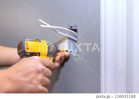 In course of renovating residence, professional electrician connects an electric socket to wall 116033188