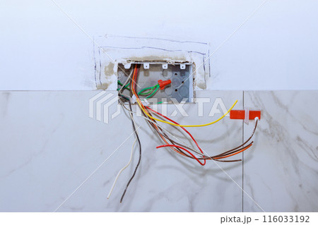 Professional electrician working connection electric socket in wall of on home electrical system during renovation 116033192