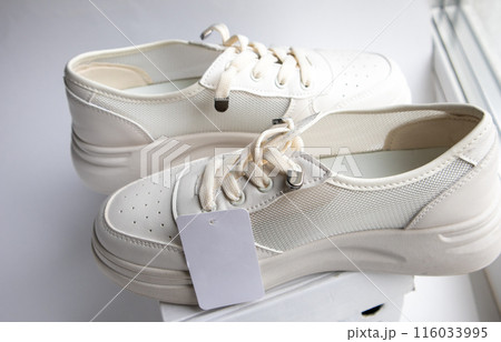 A close-up of a stylish pair of white women's sneakers with a label that has a place for your logo 116033995