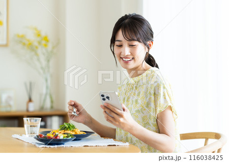 自宅でパスタを食べながらスマホを見る若い女性 自宅でパスタを食べながらスマホを見る若い女性 116038425