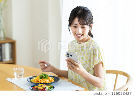 自宅でパスタを食べながらスマホを見る若い女性 自宅でパスタを食べながらスマホを見る若い女性 116038427
