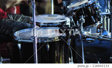 A complete drum kit for a single drummer including a variety of drums, cymbals and other percussion instruments. Black drum kit on stage. 116043133