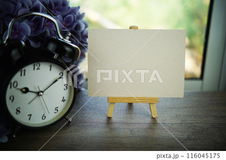 Empty card space for text message with wooden easel and alarm clcok on wooden background 116045175