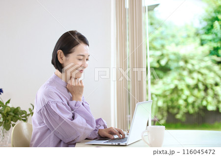 リビングでコーヒーを飲みながらパソコンを見るミドル女性 116045472