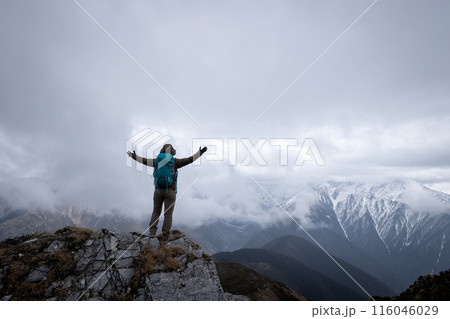Woman hiker enjoy the view on mountain top cliff edge face the snow capped mountains in tibet Woman hiker enjoy the view on mountain top cliff edge face the snow capped mountains in tibet 116046029