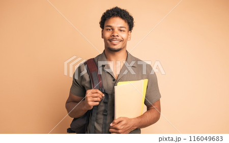 Happy male university student with backpack and books in beige studio Happy male university student with backpack and books in beige studio 116049683