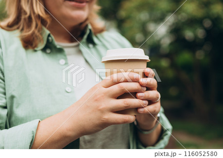 Coffee to go at autumn park. Food, rest, Take away concept. Place logo on mug, mockup. Woman hand holding brown paper cup on park background Coffee to go at autumn park. Food, rest, Take away concept. Place logo on mug, mockup. Woman hand holding brown paper cup on park background 116052580