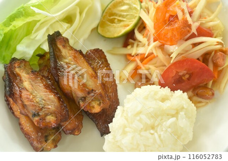 Som tum Thai spicy green papaya salad with roasted chicken wing eat couple sticky rice on plate  116052783