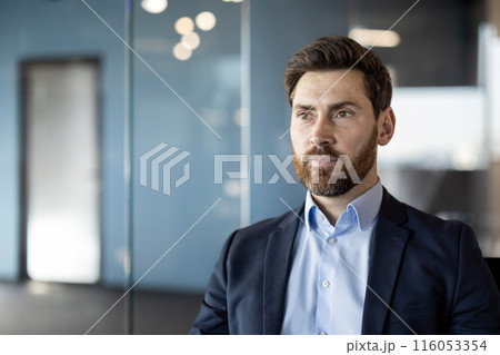 Business professional with beard and suit in modern office environment looking confident and thoughtful. Soft focus background adding depth while highlighting professional demeanor 116053354