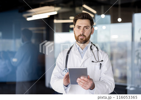 Doctor in white coat with stethoscope using digital tablet in hospital. Medical professional focused on patient data and healthcare technology. Office background with blurred colleagues. Doctor in white coat with stethoscope using digital tablet in hospital. Medical professional focused on patient data and healthcare technology. Office background with blurred colleagues. 116053365