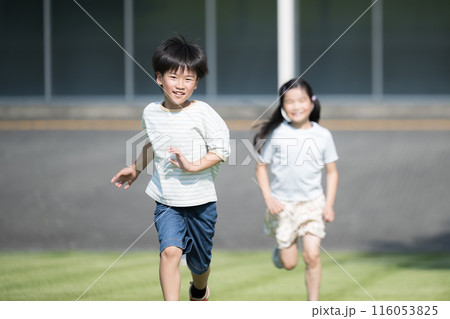 校舎を背景に芝生を走る競争する笑顔の子供(小学生)たちの様子 116053825
