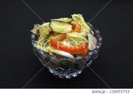 Vegetable salad in a glass salad bowl on a black background. A portion of vegetable salad. 116055732