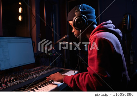 A black male singer is recording vocals in a music studio using a microphone and wearing headphones. The rap artist is recording a new album 116056890
