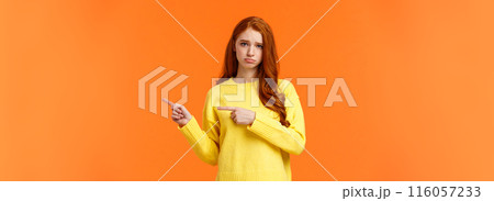Sulking moody and sad cute redhead girlfriend pointing right and frowning, standing unhappy with bad mood, envy someone, begging boyfriend book tickets for winter ski-resort, orange background Sulking moody and sad cute redhead girlfriend pointing right and frowning, standing unhappy with bad mood, envy someone, begging boyfriend book tickets for winter ski-resort, orange background 116057233